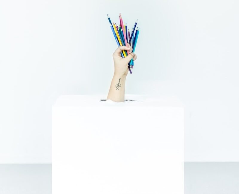 person's hand burst out of box holding assorted-color pens